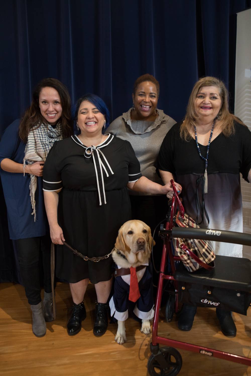 Group photo of four women, one with her service dog and another with a walker. They are all smiling